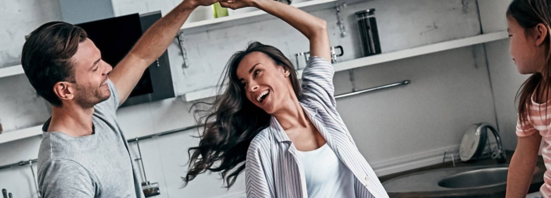Dansend stel in keuken terwijl kind toekijkt zittend op aanrecht 