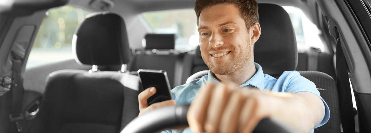 Een man is in een auto aan het rijden en grbuikt tijdens het rijden zijn mobiele telefoon
