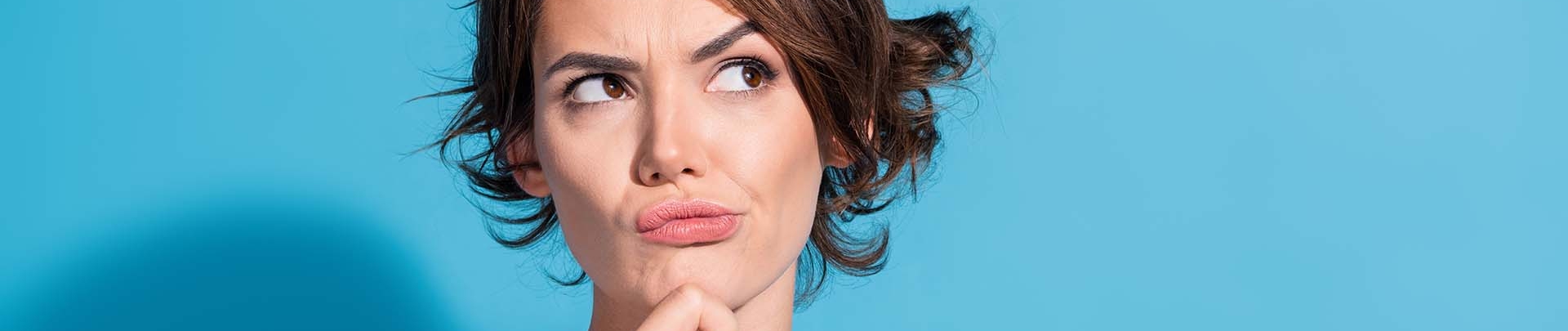 Denkende vrouw met haar hand op haar kin draagt een roze satijnen blouse en stata voor een blauwe achtergrond